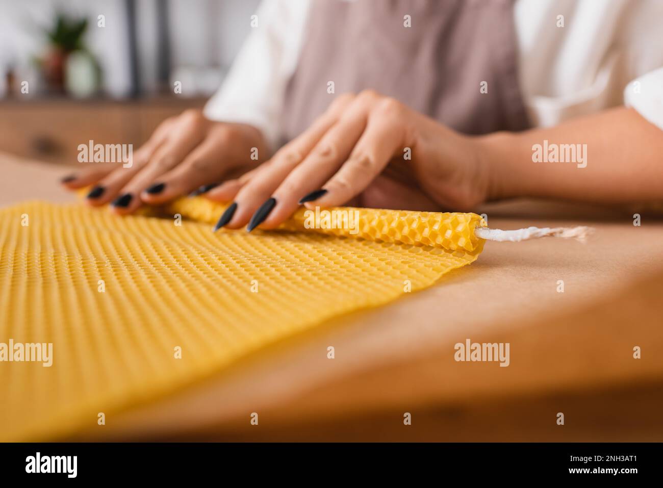 partial view of african american craftswoman making natural candle and rolling wax sheet on blurred parchment in workshop,stock image Stock Photo
