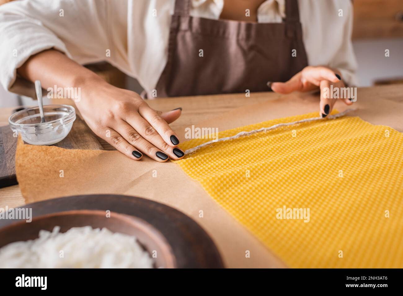 partial view of african american woman in apron holding natural twine near wax sheet on parchment in craft workshop,stock image Stock Photo