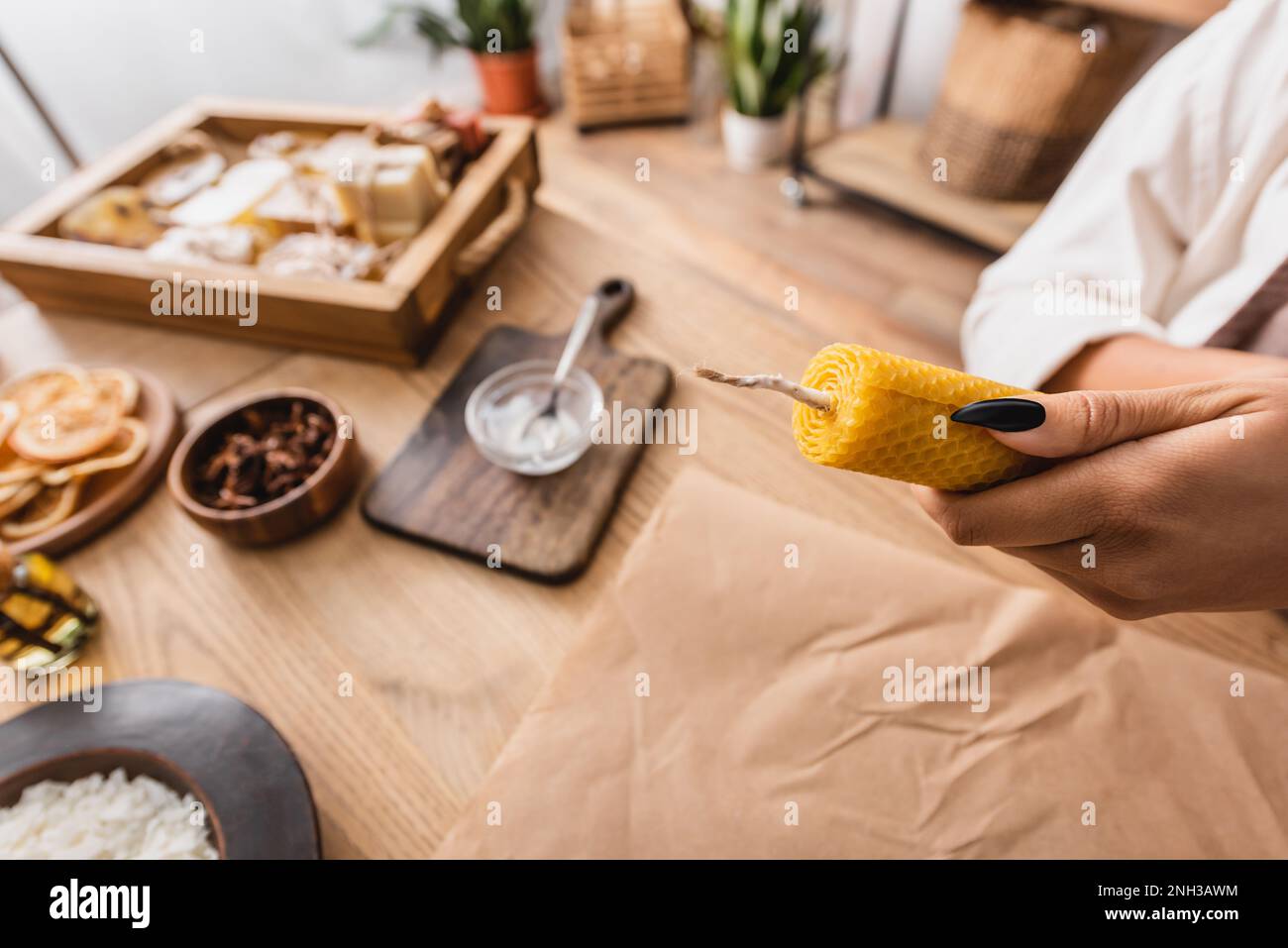 partial view of african american craftswoman holding handmade candle near parchment and natural ingredients on wooden table,stock image Stock Photo