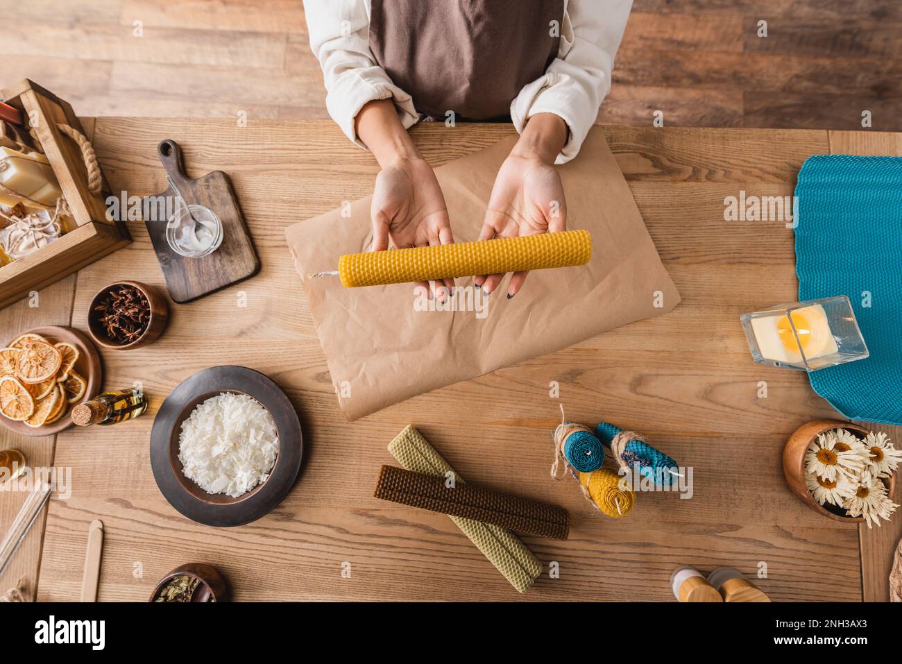 top view of cropped african american woman holding handmade candle near parchment and natural ingredients in craft workshop,stock image Stock Photo