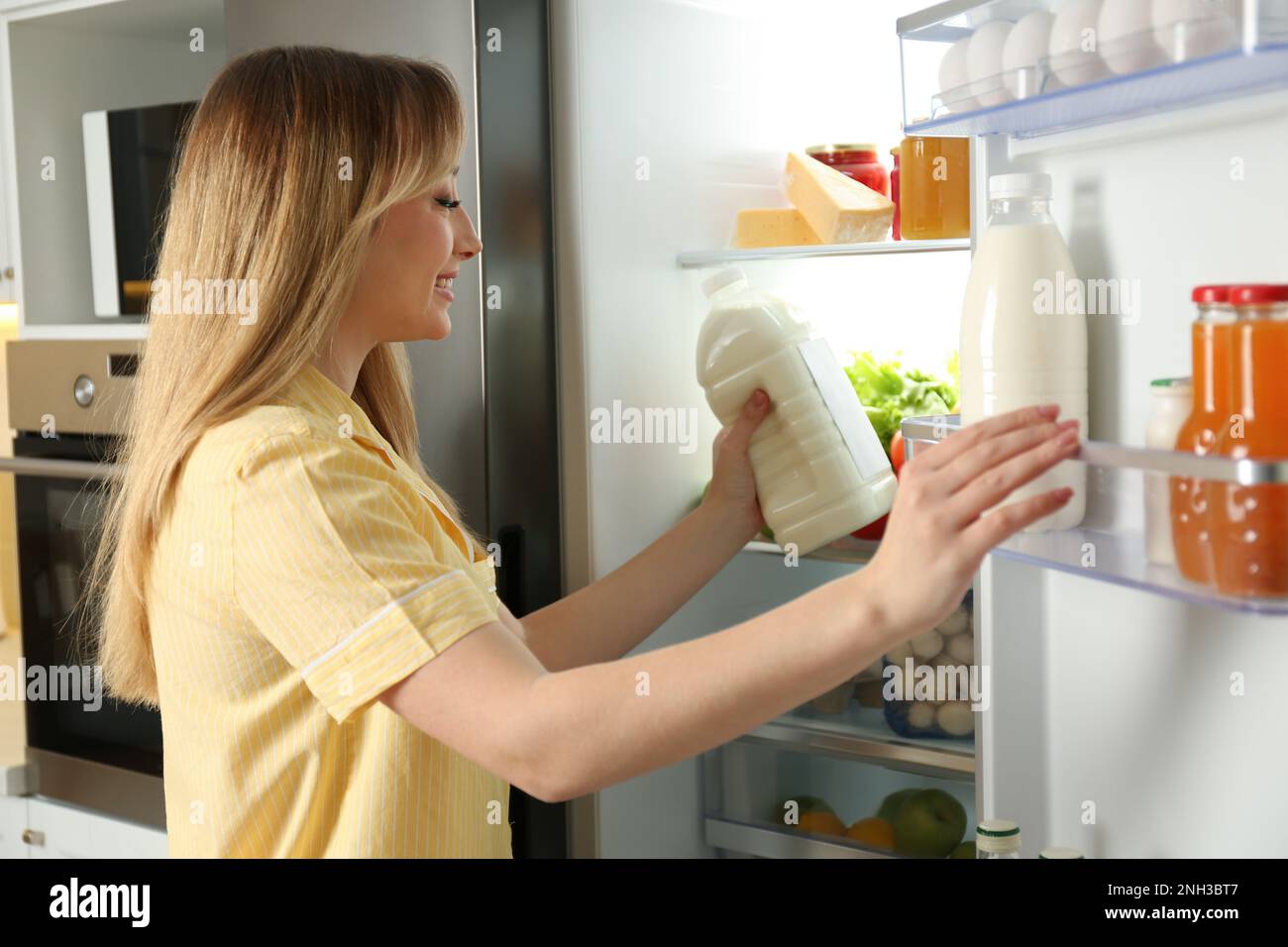 https://c8.alamy.com/comp/2NH3BT7/young-woman-putting-gallon-of-milk-into-refrigerator-in-kitchen-2NH3BT7.jpg