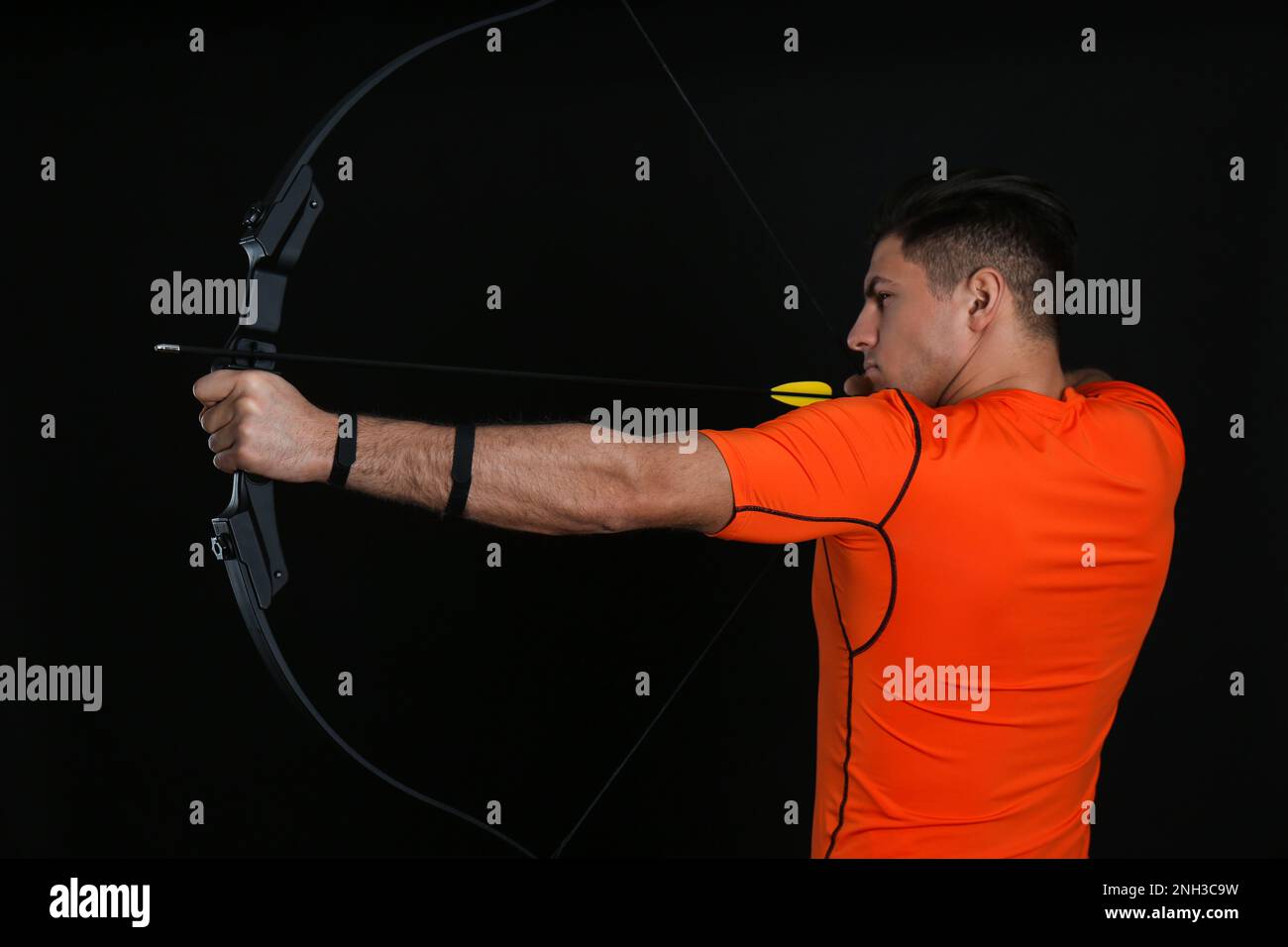 Man with bow and arrow practicing archery on black background Stock Photo