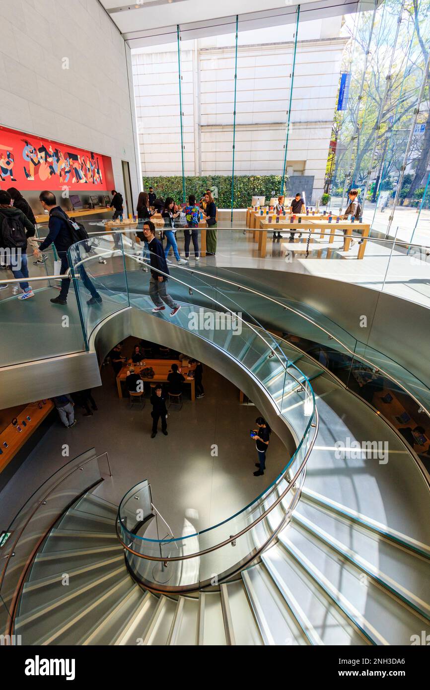 Interior of the Apple store in Omotesando, Tokyo. Center spiral staircase to basement level, while on ground floor people looking at i-phones. Stock Photo