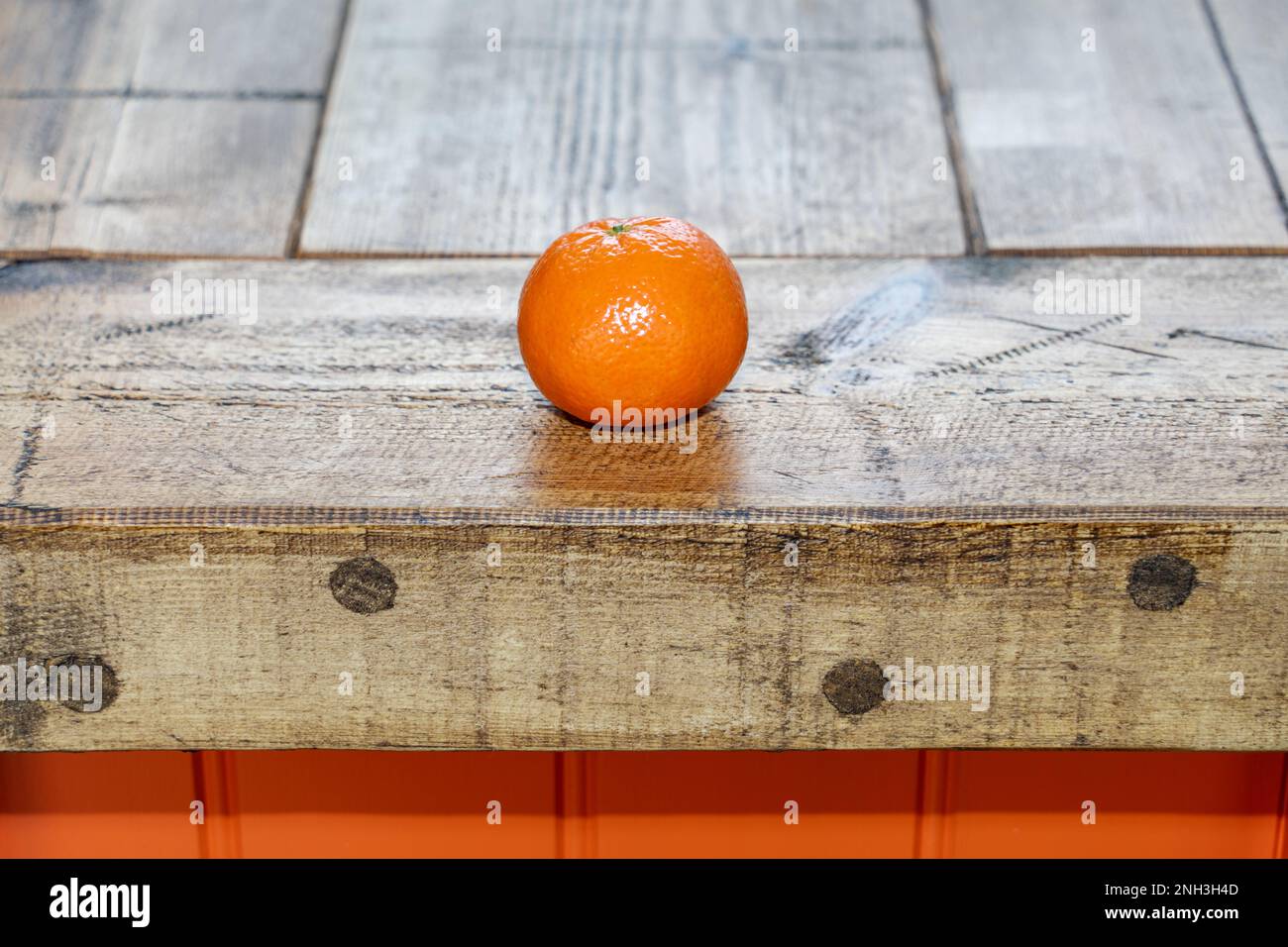 An organic satsuma on the edge of a rough wooden butcher's block with orange sides. Concept of healthy eating lifestyle kitchen. Stock Photo