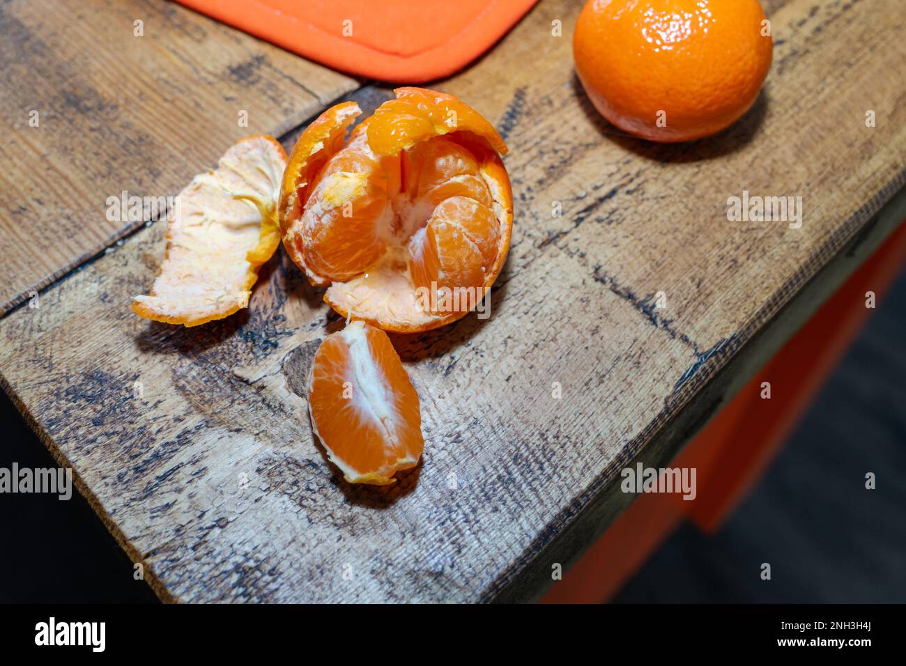 Two organic satsumas. one opened, on the edge of a rough wooden butcher's block with orange sides. Concept of healthy eating lifestyle kitchen. Stock Photo
