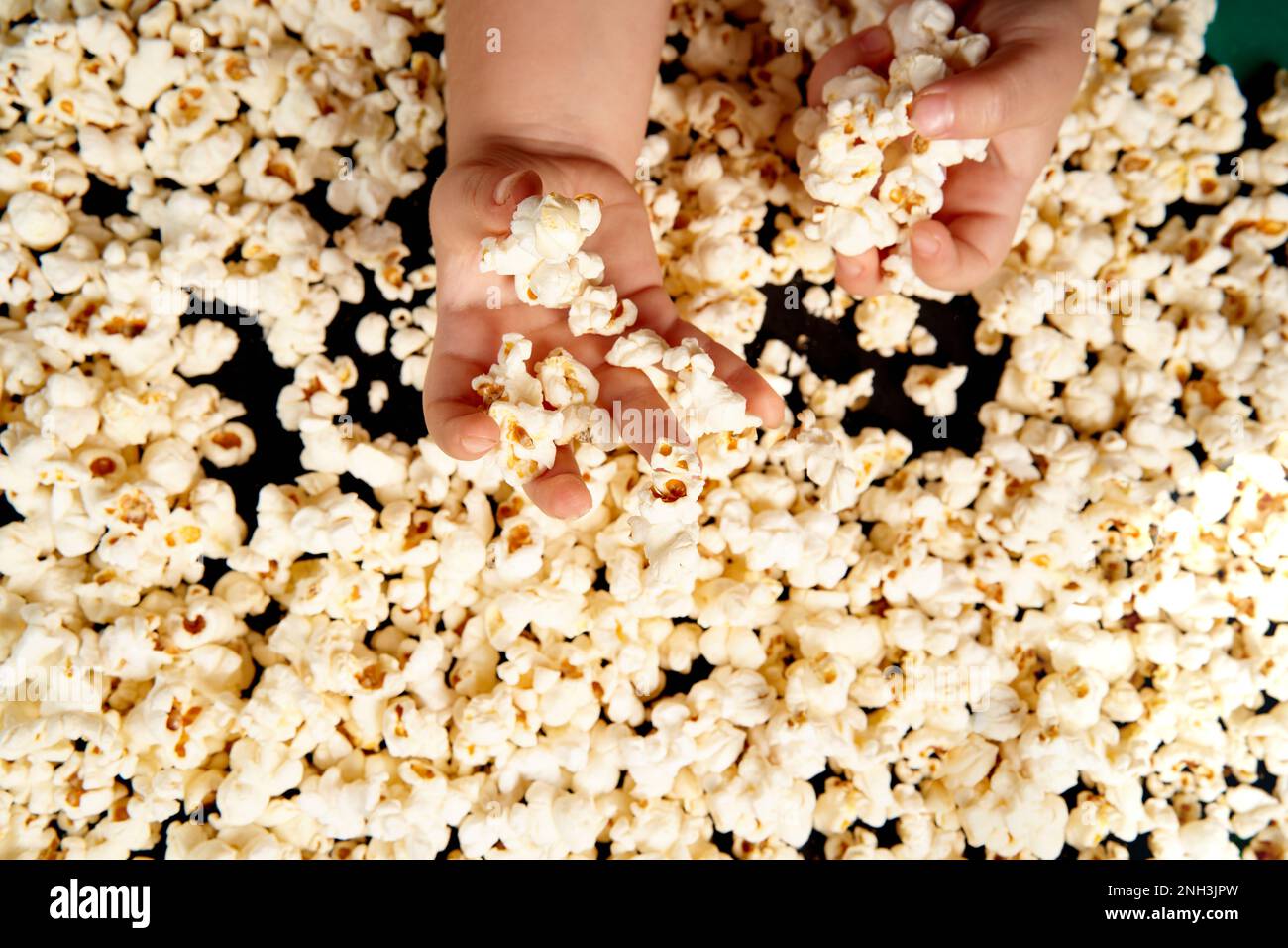 Children's hands are picking up popcorn. Flat lay . The concept of a birthday, party, holiday, home leisure. Copy space for your product. Popcorn texture or background. Stock Photo