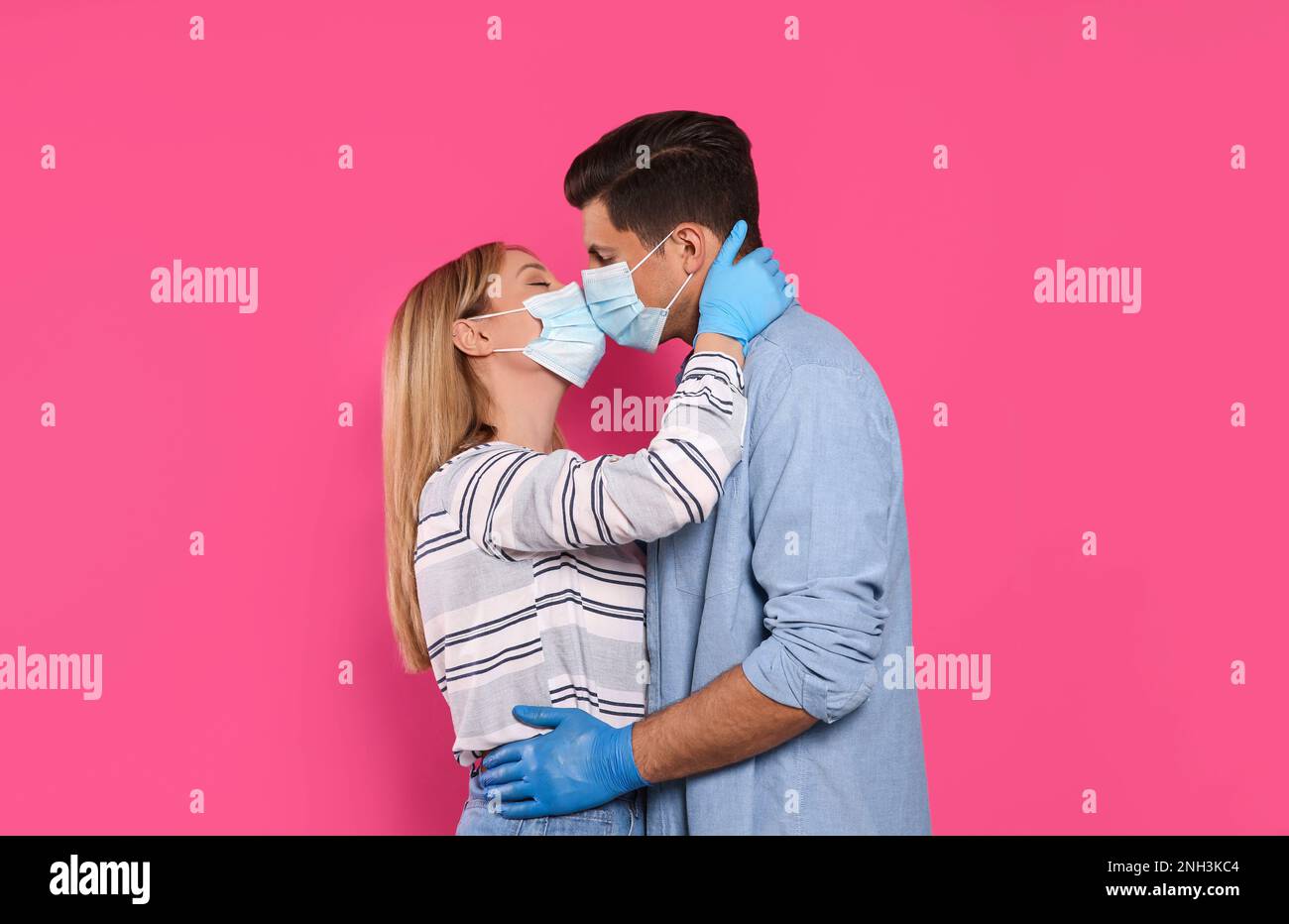 Couple in medical masks and gloves trying to kiss on pink background ...