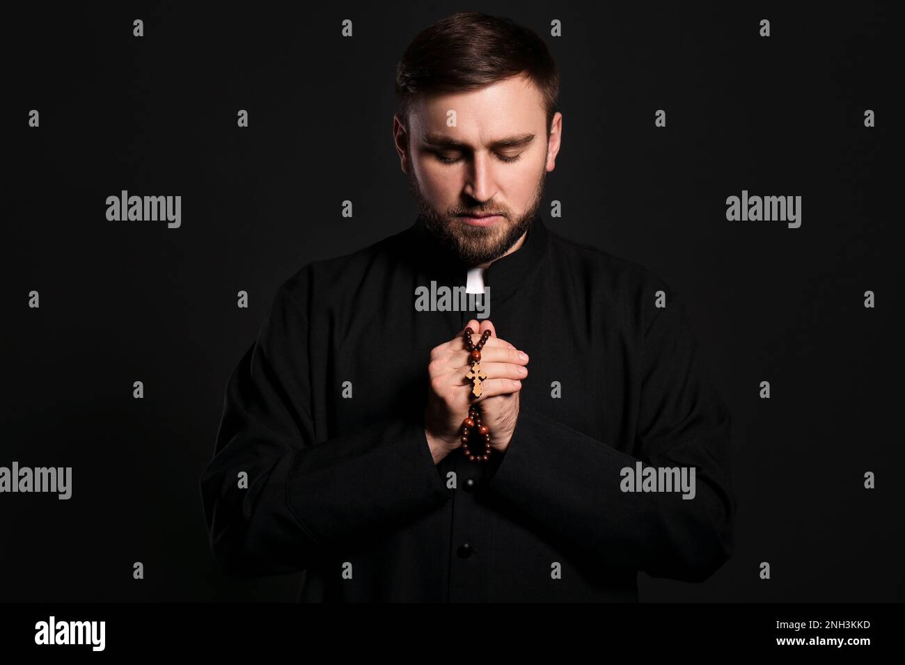 Priest with rosary beads praying on black background Stock Photo