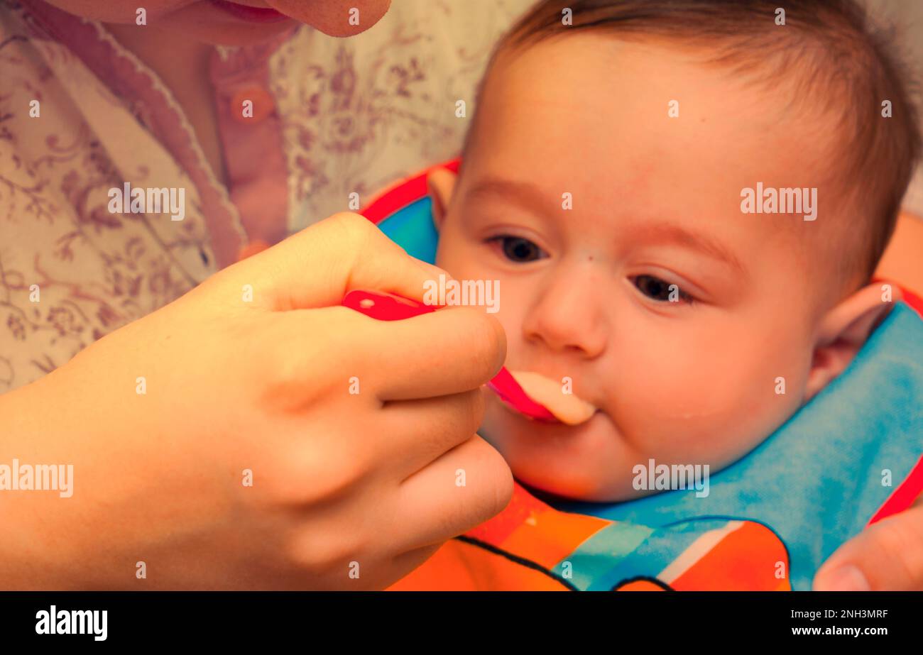 Woman's hand feeding food to little baby boy.New born baby boy wearing napkin while eating cereal. Stock Photo