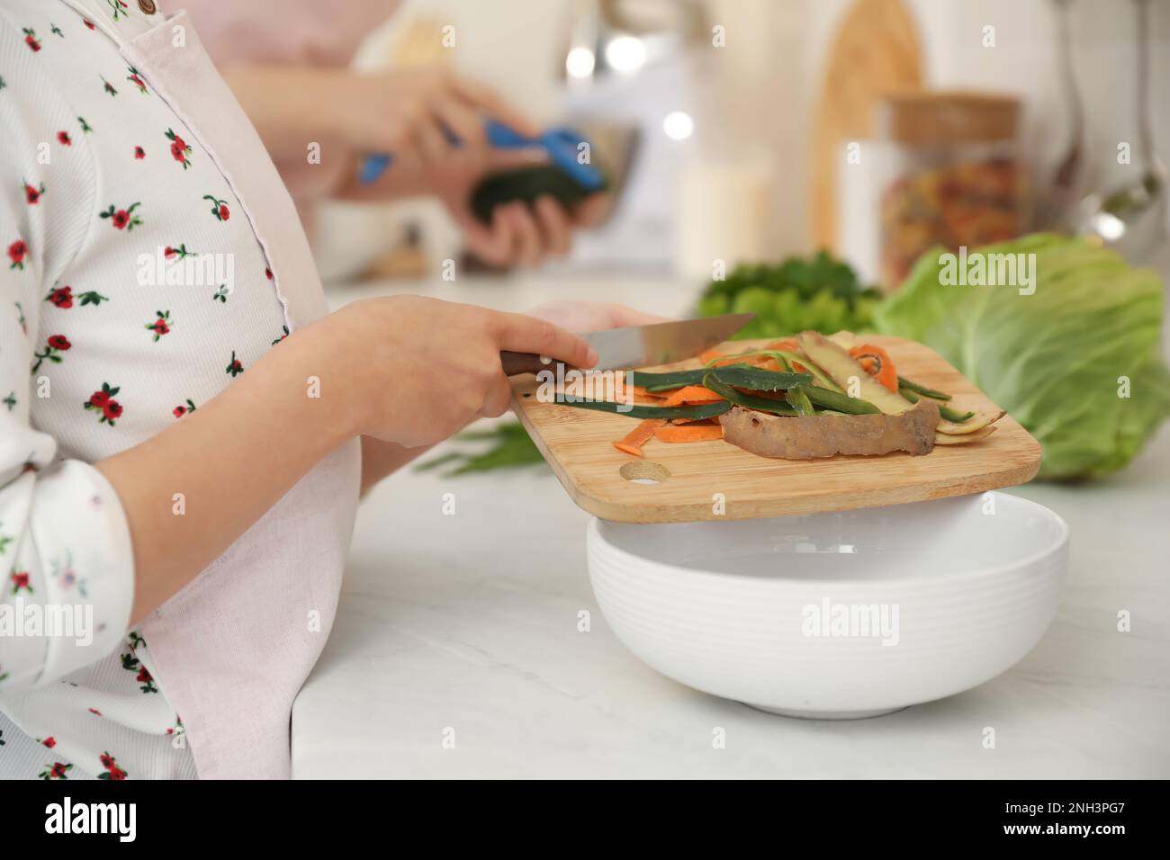 Little girl with cutting board and knife scraping vegetable peels into