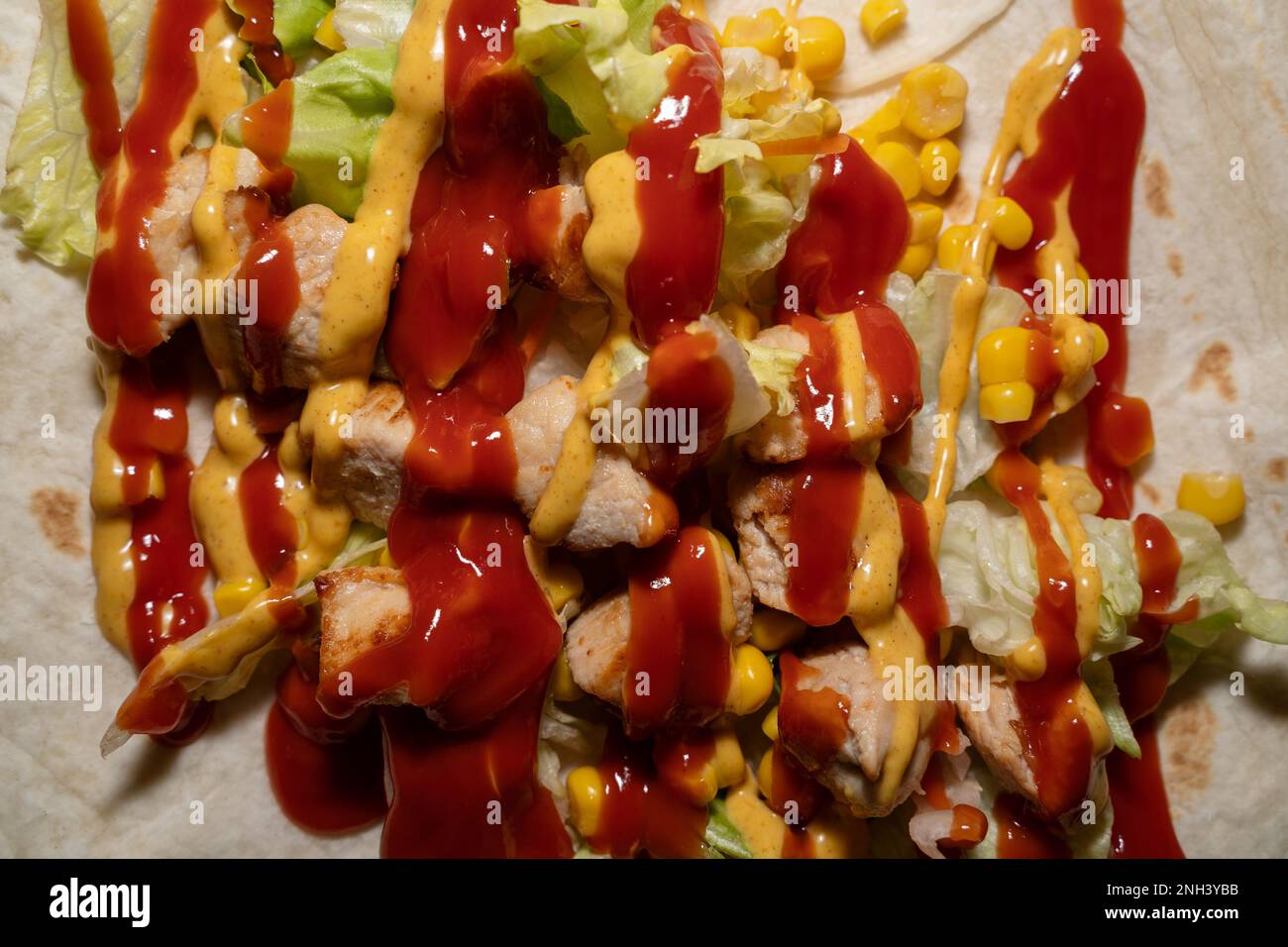 Close up of a wrap with lettuce, sweet corn, chicken, ketchup and
