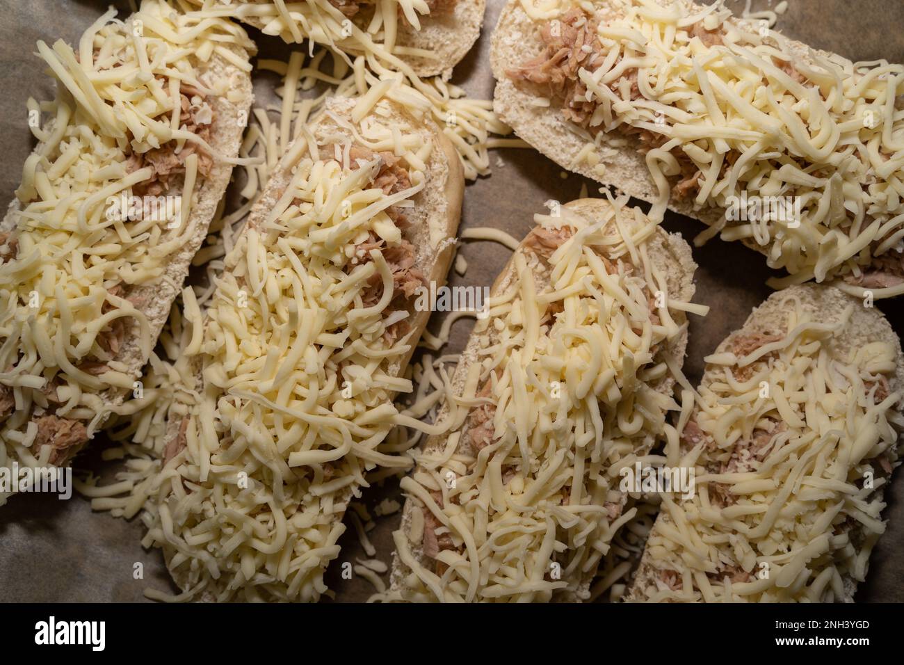 Top view of many unbaked sandwiches with tuna and cheese on a baking