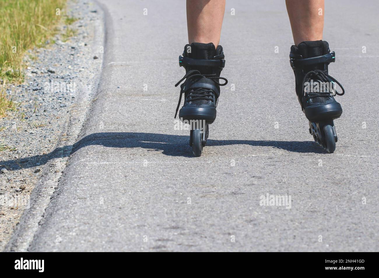 Legs of woman who is learning of inline skating on asphalt road Stock