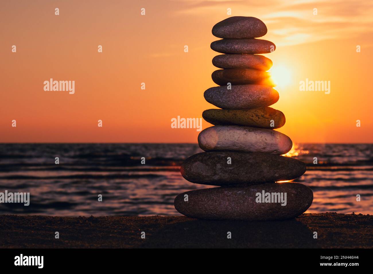 Stacked rocks on the beach with a sunset ocean in the background, Zen Sunset Wallpapers, Pyramid of pebbles on the beach at sunset. Stock Photo