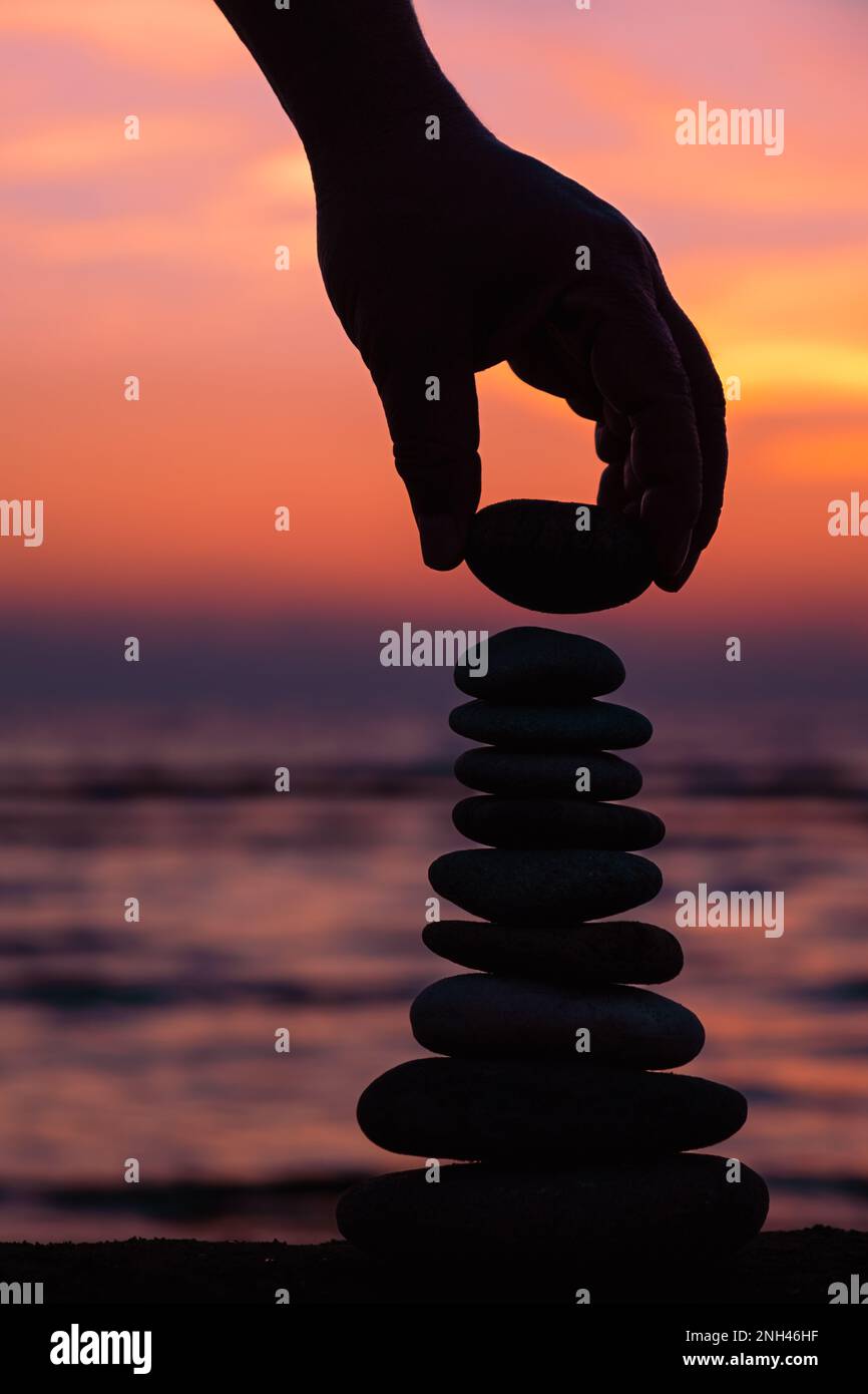 Vertical İmage of stacking rocks on the beach with a sunset ocean in the background, Zen Sunset Wallpapers, Pyramid of pebbles on the beach at sunset. Stock Photo