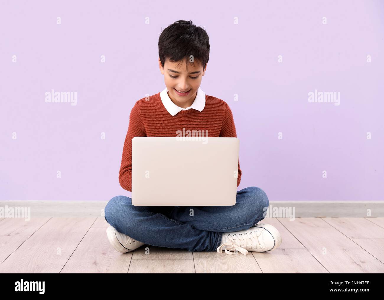 Little boy using laptop near lilac wall Stock Photo - Alamy