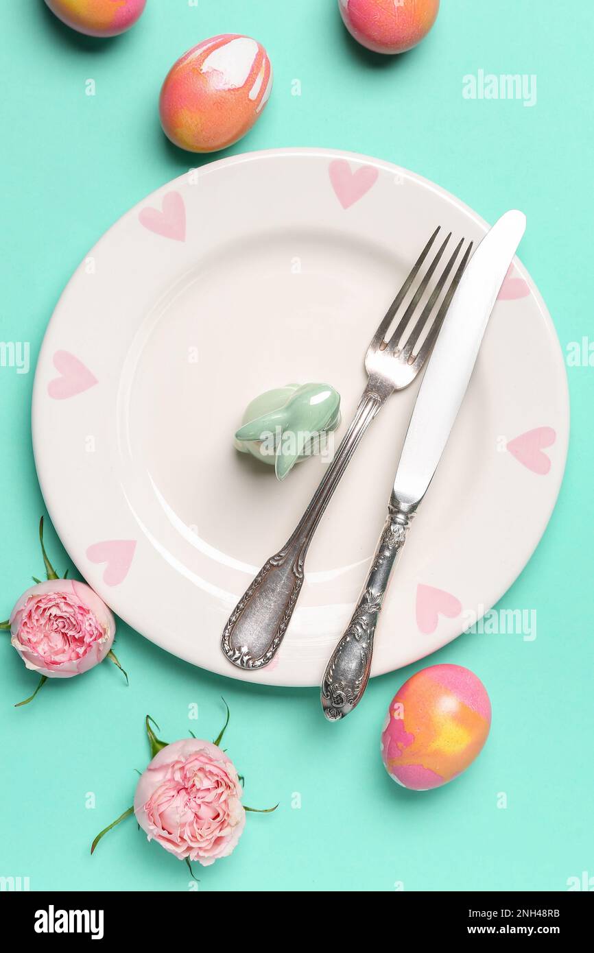 Table setting with Easter rabbit, eggs and flowers on mint background Stock Photo