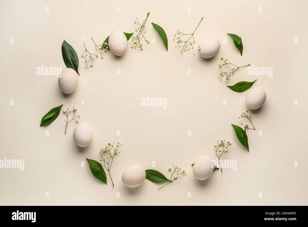 Frame made of Easter eggs, green leaves and gypsophila flowers on white ...
