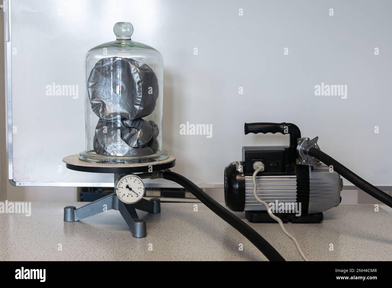 Inflatable doll under a bell jar is vacuum sucked by a pump. The doll