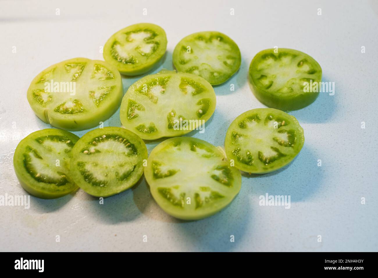 Fresh green tomato slices on a white background ready for breading and frying.  Kansas, USA. Stock Photo