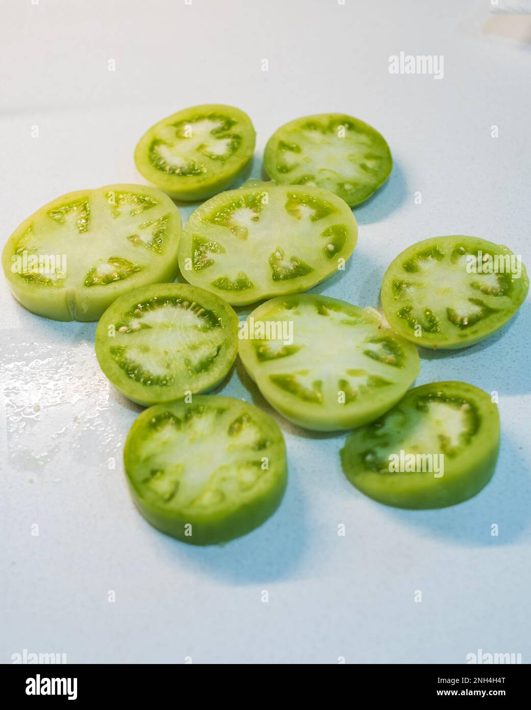 Sliced green tomatoes ready for breading and frying on a white background . Stock Photo