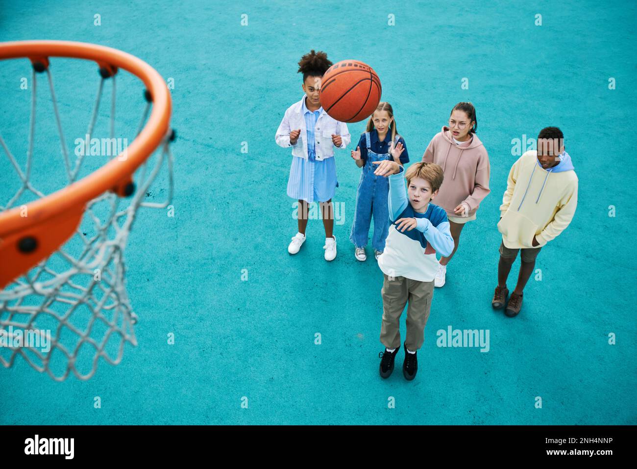 Above angle of intercultural schoolchildren playing basketball on playground together while one