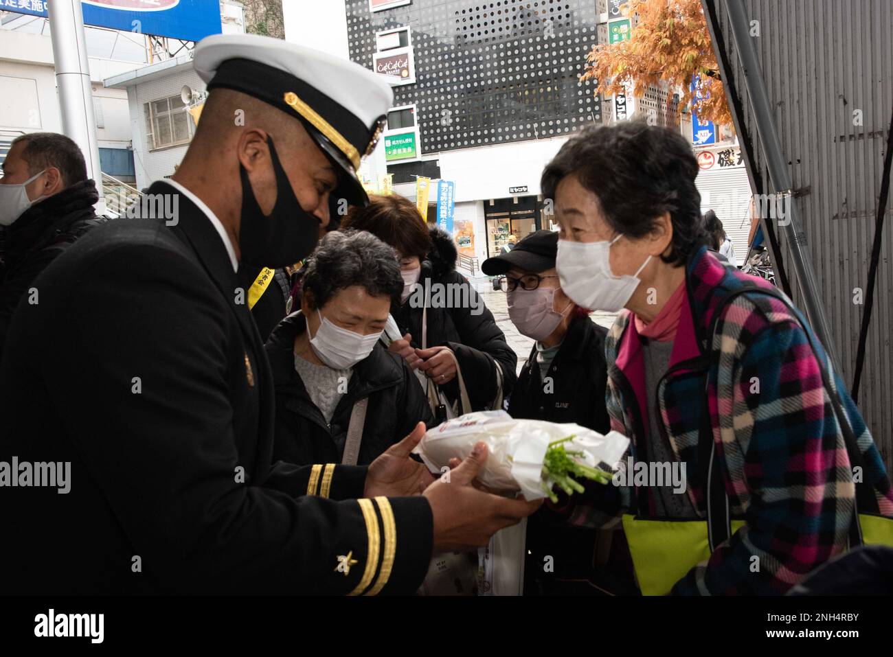 YOKOSUKA, Japan (Dec. 13, 2022) — Lt. Alexander Bates, security officer at Commander, Fleet Activities Yokosuka (CFAY) hands out a Japanese daikon radish to a pedestrian at Yokosuka Chuo Station during an event raising awareness of drunk driving during the holiday season. “Daikon” is a play on words as it is close to the Japanese word “daikonzetsu”, meaning eradication (of drunk driving). For more than 75 years, CFAY has provided, maintained, and operated base facilities and services in support of the U.S. 7th Fleet’s forward deployed naval forces, tenant commands, and thousands of military an Stock Photo