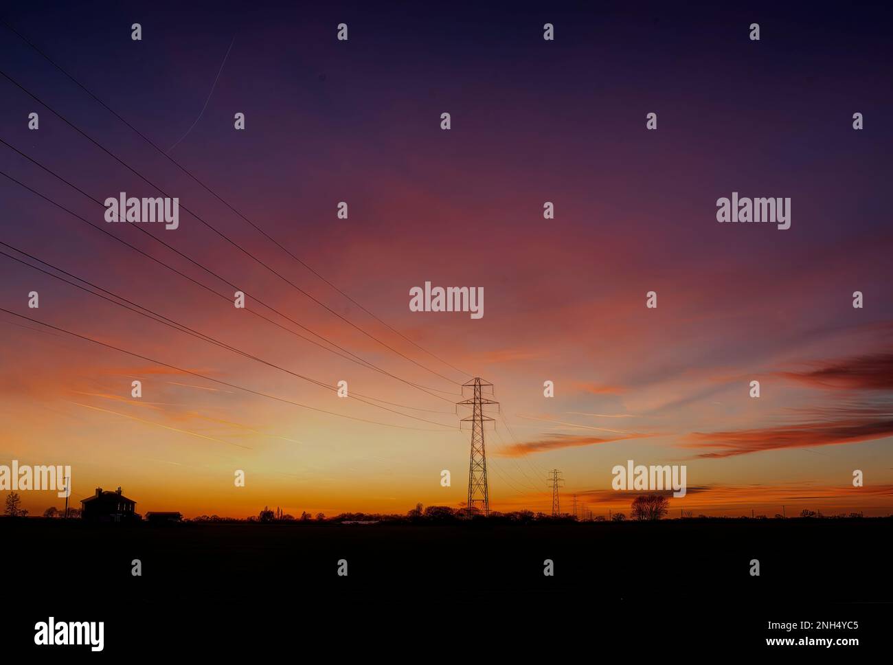 The silhouette of electricity pylons at sunset in rural Essex, UK Stock Photo