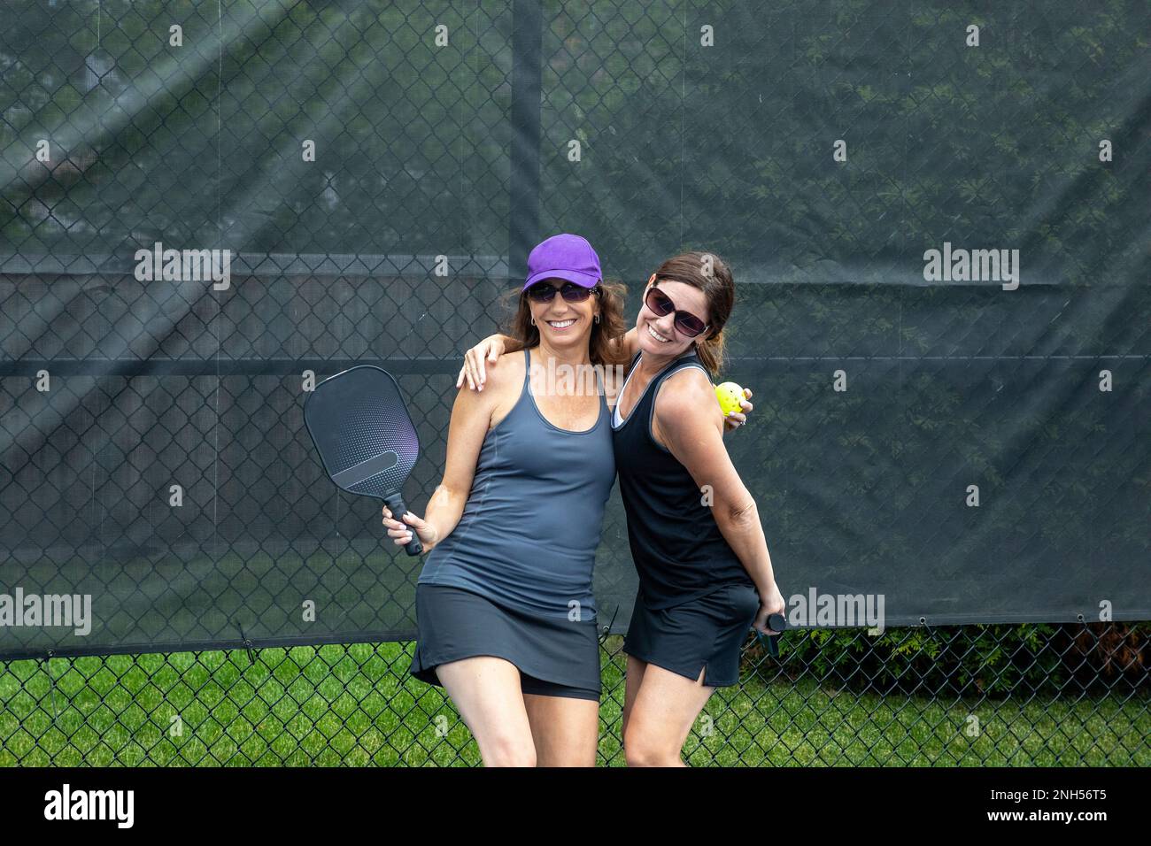 Two pickleball players posing with paddles on a court during summer