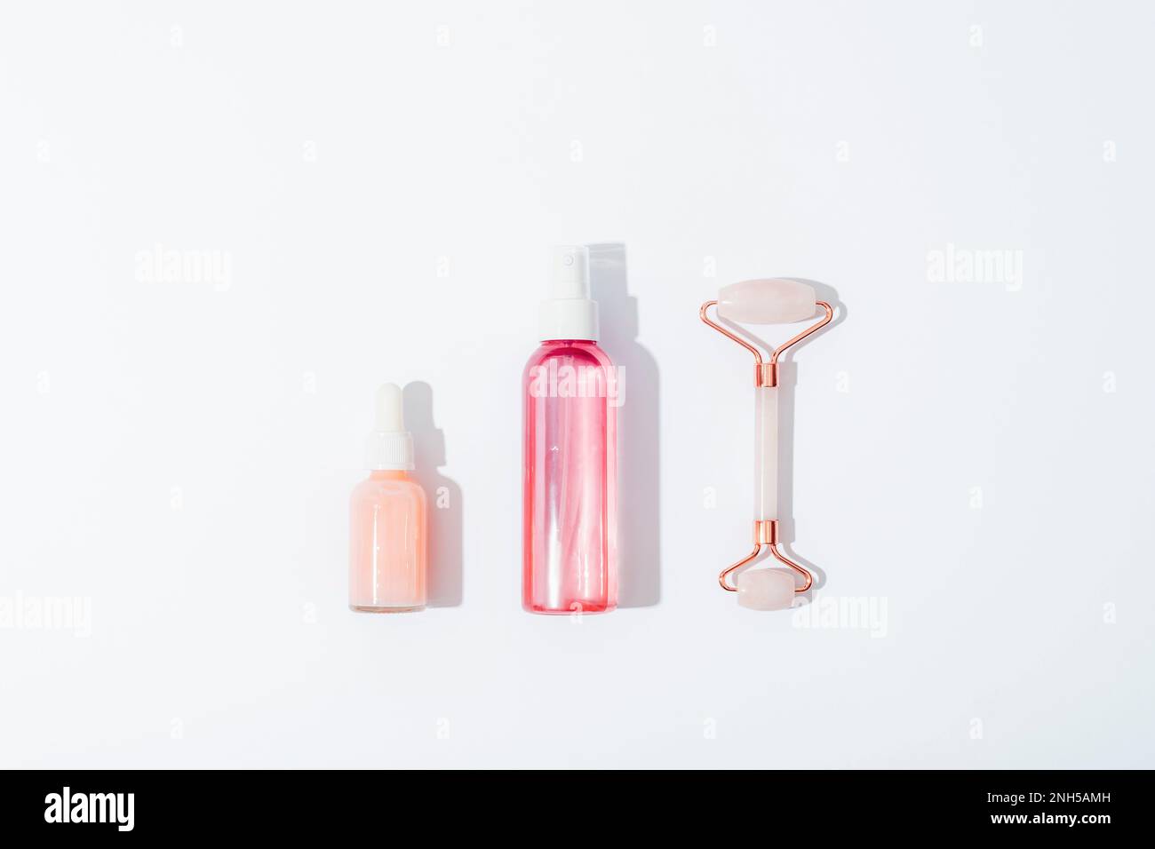 Pink cosmetic bottles and rose quartz crystal facial roller on white