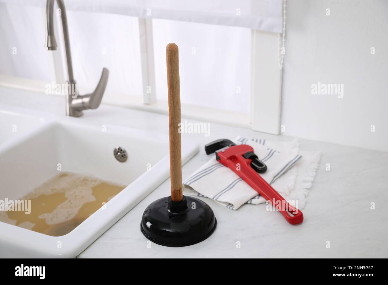 https://c8.alamy.com/comp/2NH5G67/plunger-pipe-wrench-and-towel-on-kitchen-counter-near-clogged-sink-2NH5G67.jpg