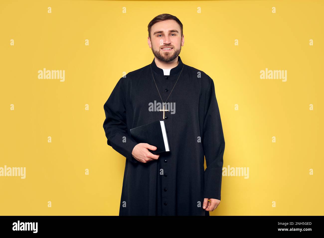 Priest in cassock with Bible on yellow background Stock Photo
