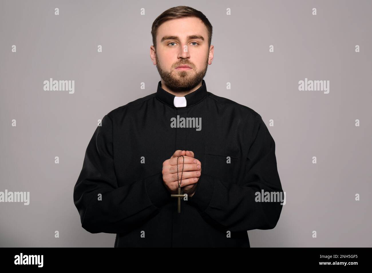 Priest in cassock with cross on grey background Stock Photo