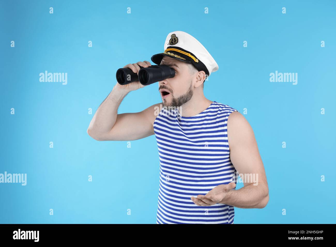 Sailor looking through binoculars on light blue background Stock Photo
