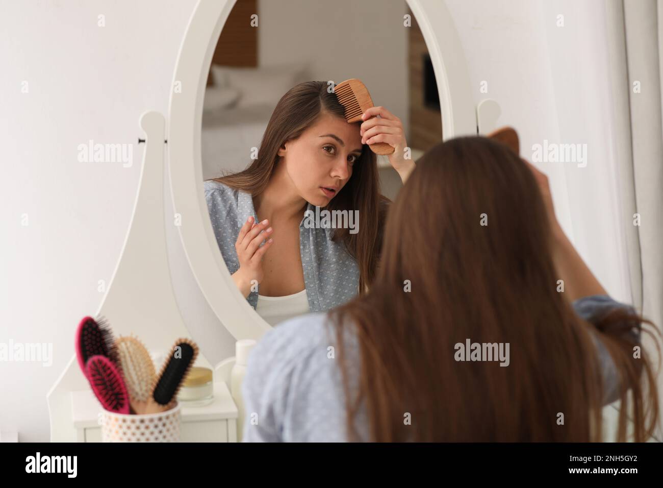 Young woman with hair loss problem near mirror indoors Stock Photo