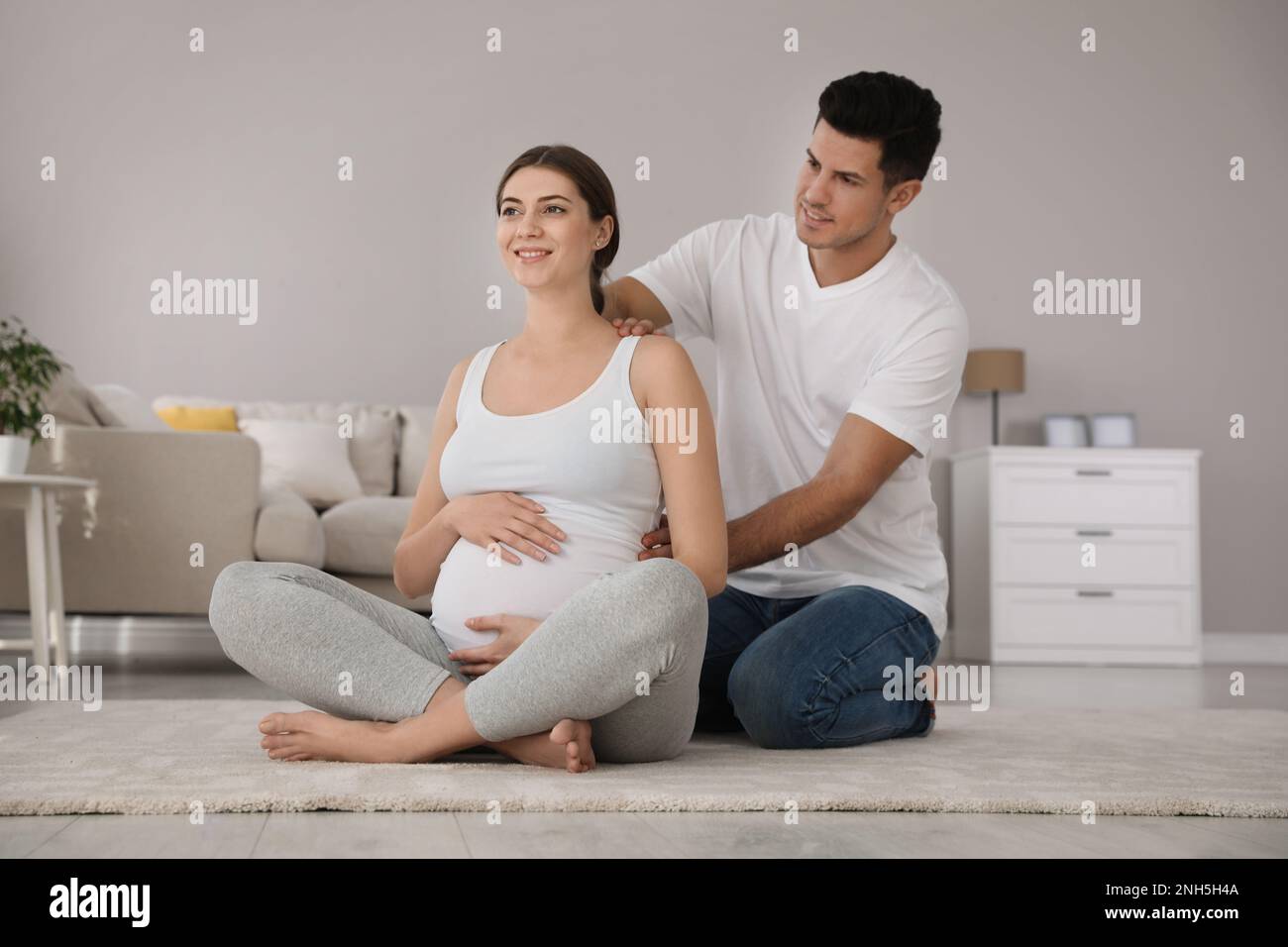 Husband Massaging His Pregnant Wife In Light Room Preparation For