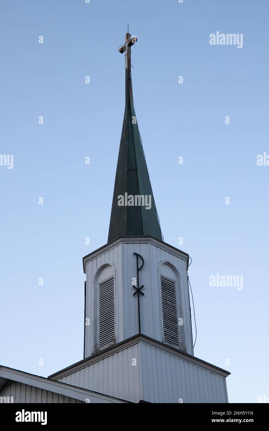 St. Joseph's  Catholic Church Steeple with a Pax Christi Symbol on it and a cross at the top. White with a grey top. Stock Photo