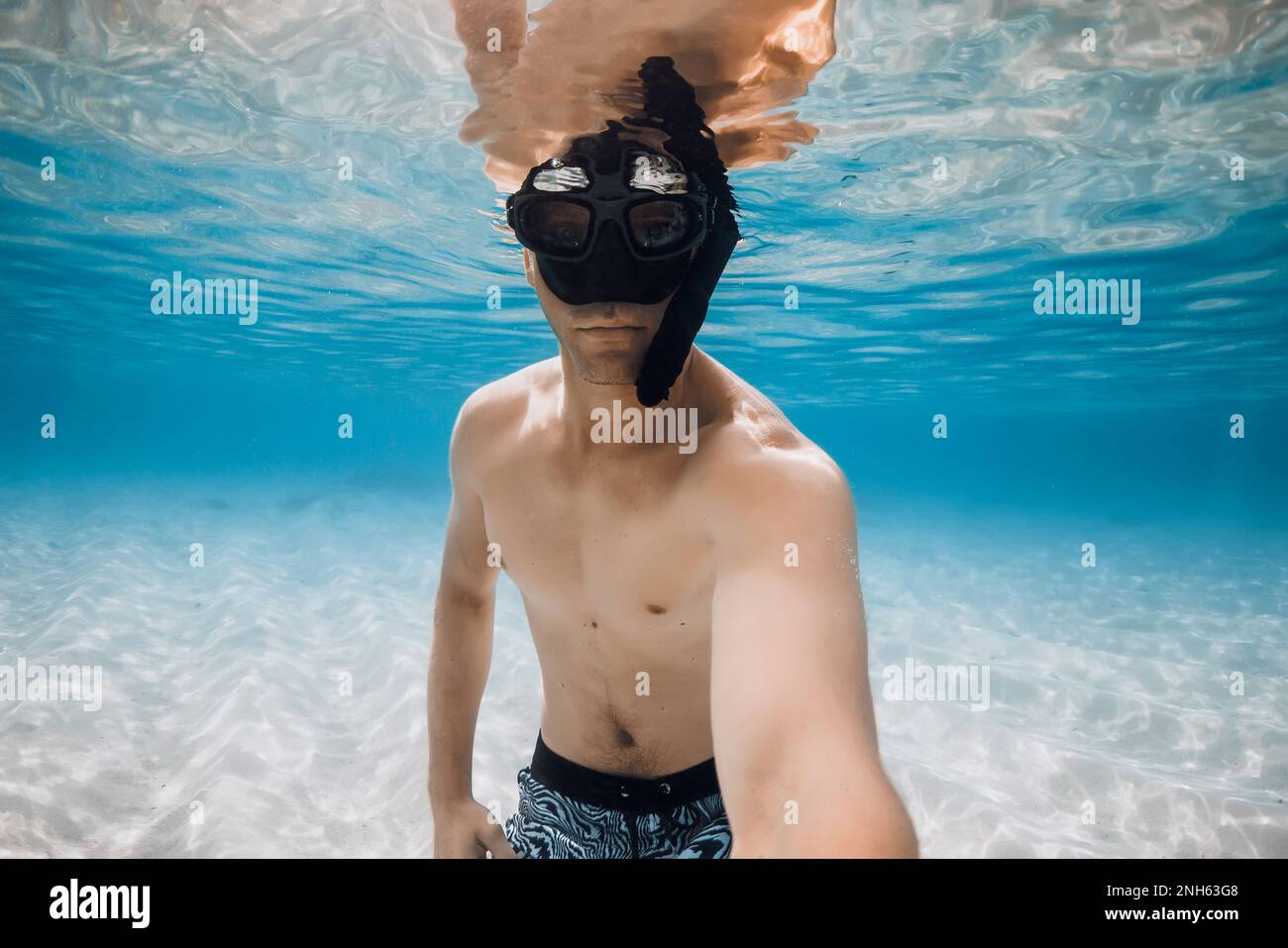 Man freediver in diving mask make selfie underwater over sandy bottom
