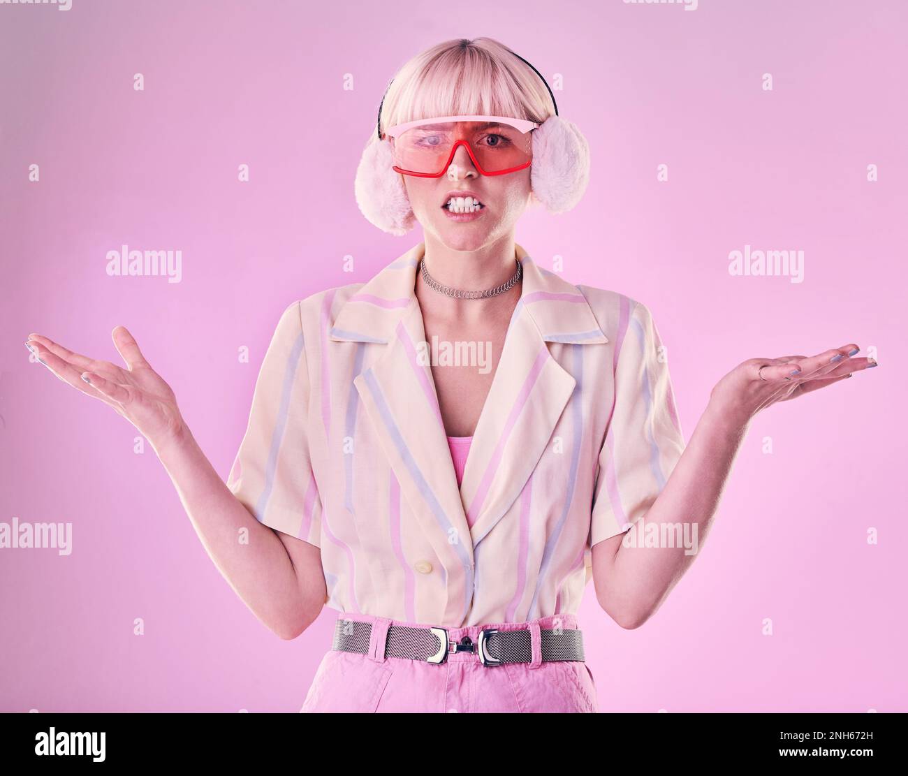 Confused, angry and portrait of a woman with fashion isolated on a pink background in a studio. Anxiety, sad and stylish girl model wearing ear muffs Stock Photo