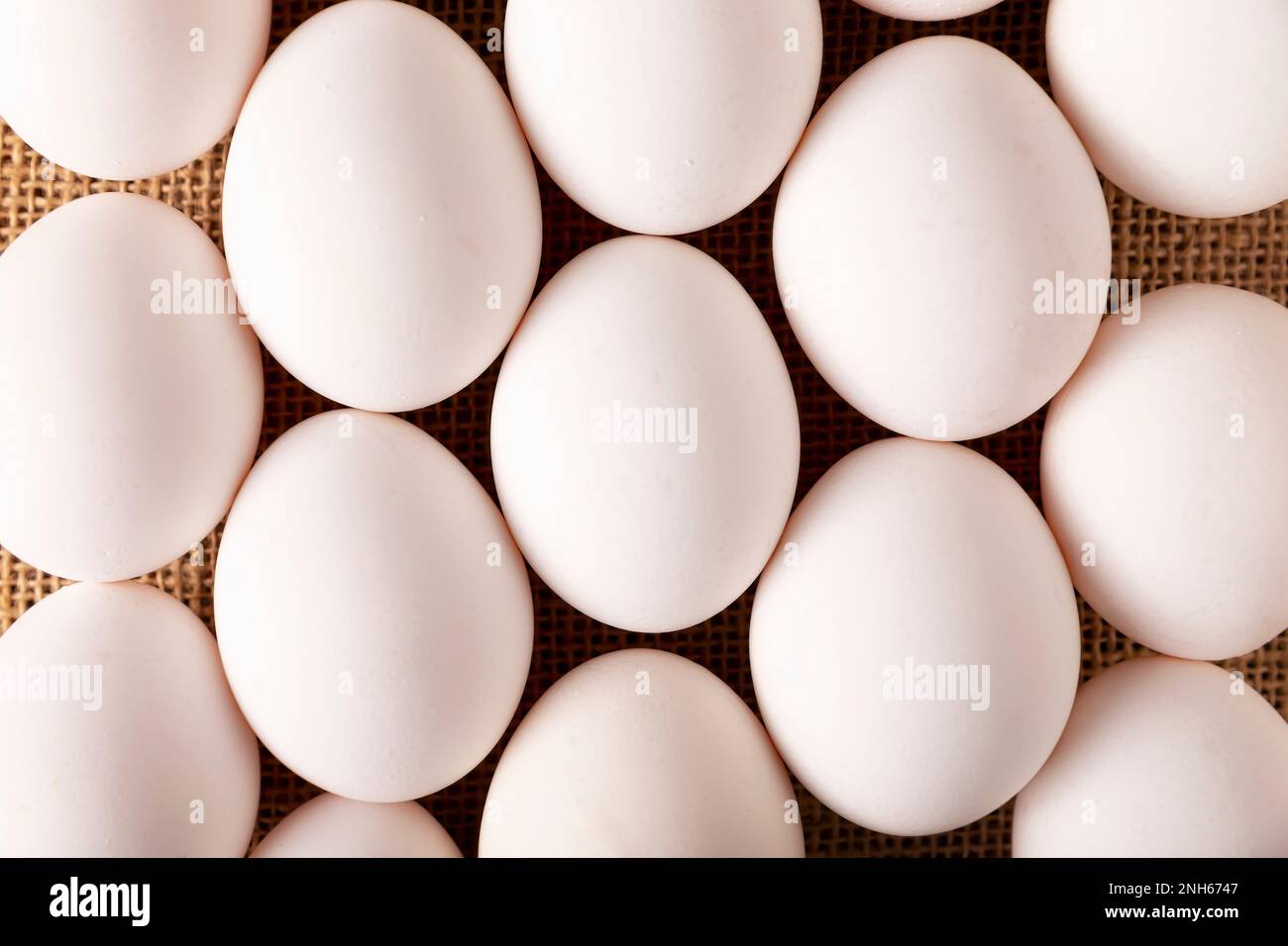 White chicken eggs arranged on burlap texture. Very popular nutritious and economic food product. Top table view. Stock Photo