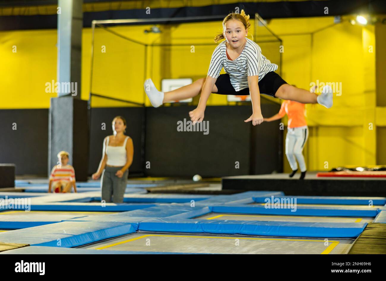 Cheerful girl bouncing spreading her legs on trampolines during free time on weekends at