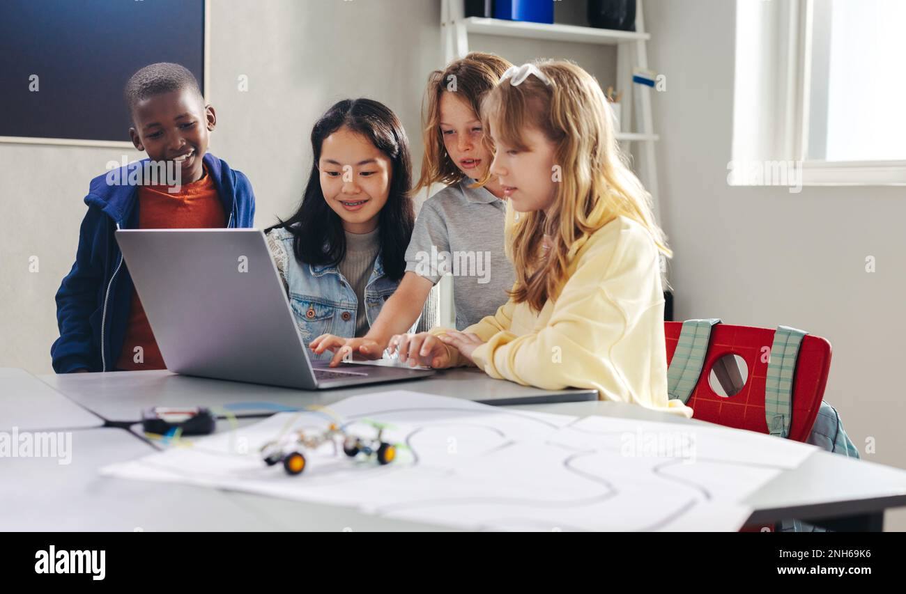 Group of diverse school kids learning how to program robots using a laptop. Elementary school students developing coding skills to control robot cars Stock Photo