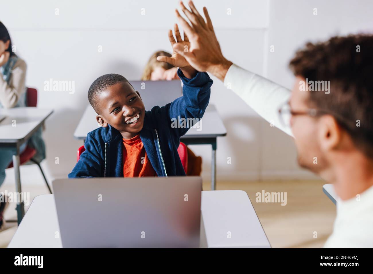 Happy black kid doing a high five with his teacher in a computer science classroom, celebrating a successful teaching and learning moment. Young stude Stock Photo
