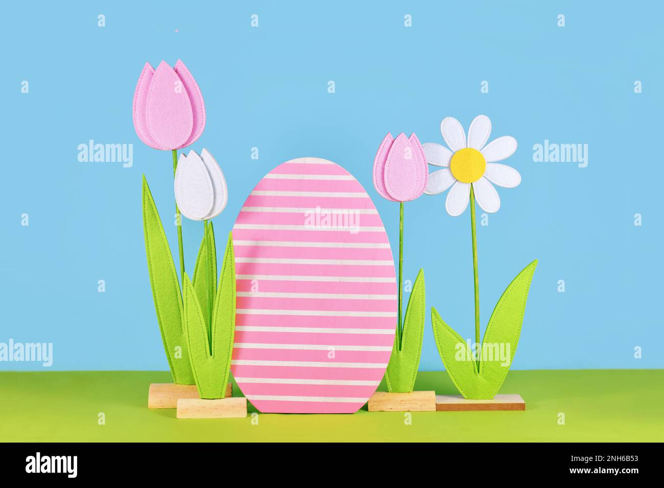 Easter arrangement with felt spring flowers and wooden easter egg in front of blue background Stock Photo