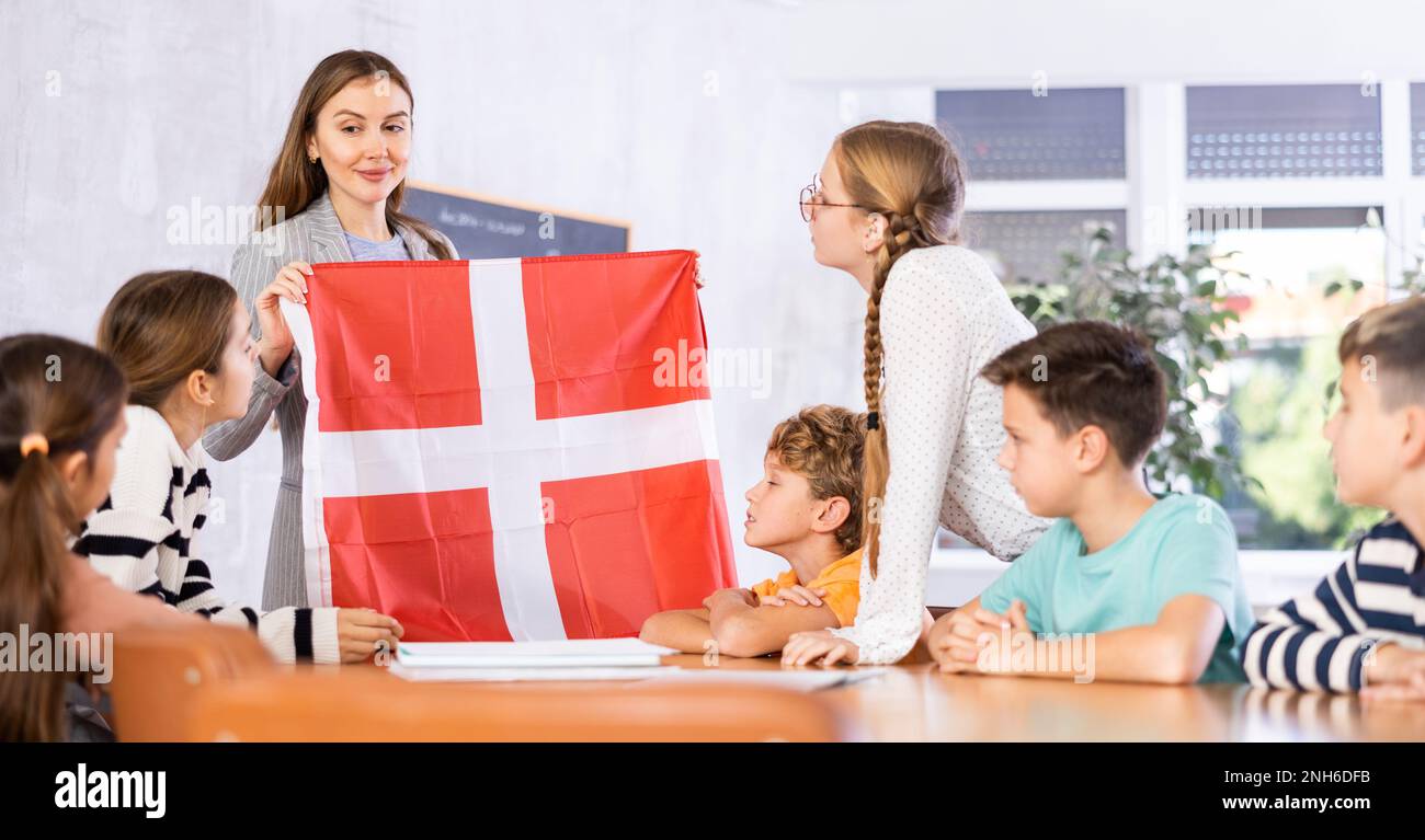 School teacher tells students about Denmark and holds a Denmark flag in hands. Stock Photo