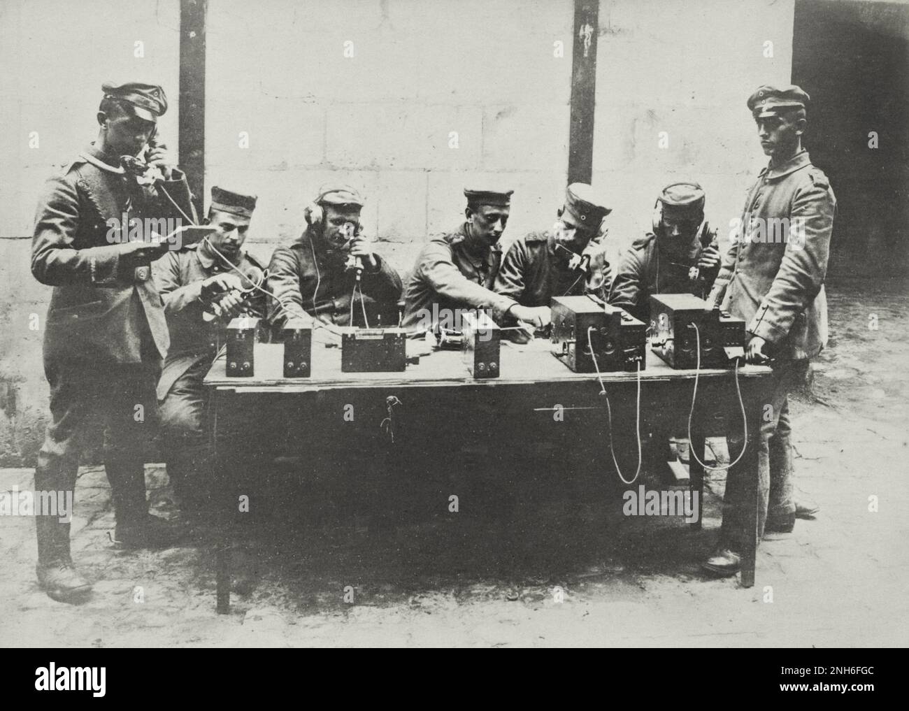 The picture shows a group of soldiers sitting around a table with telephone sets and making phone calls. The man on the right appears to be an officer standing guard. On the left side is also an officer who has taken over a call. Stock Photo