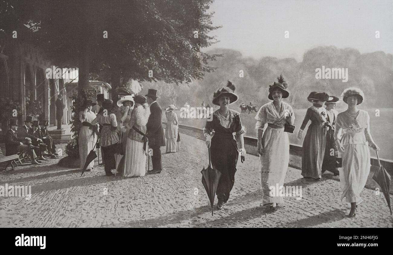 Paris seasons. Late afternoon at the Polo de Bagatelle. Paris, France. July 1913 It is on one of those sweet afternoons, when it is so pleasant to extend the time of the au Bois until the evening meal, conducive to light talks and elegant meetings... Among all the 'appointments' of good company, the Polo de Bagetelle, near Longchamp, offers itself as one of the most chosen. While, on the vast grass carpet reserved for the game, a rough race continues, among the gallopades and the blows of the mallet, peaceful groups wander along the fine sandy alley, or sit under the trees, opposing, in contra Stock Photo