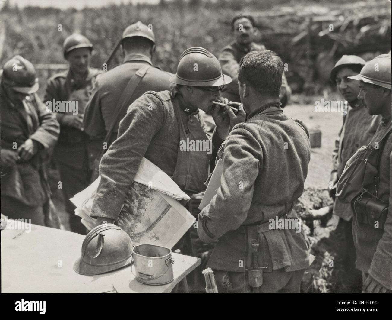 World War I. Italian soldier holding illustrated newspaper gets his cigarette lit by another soldier near Piave River, Italy. October 1918 Stock Photo