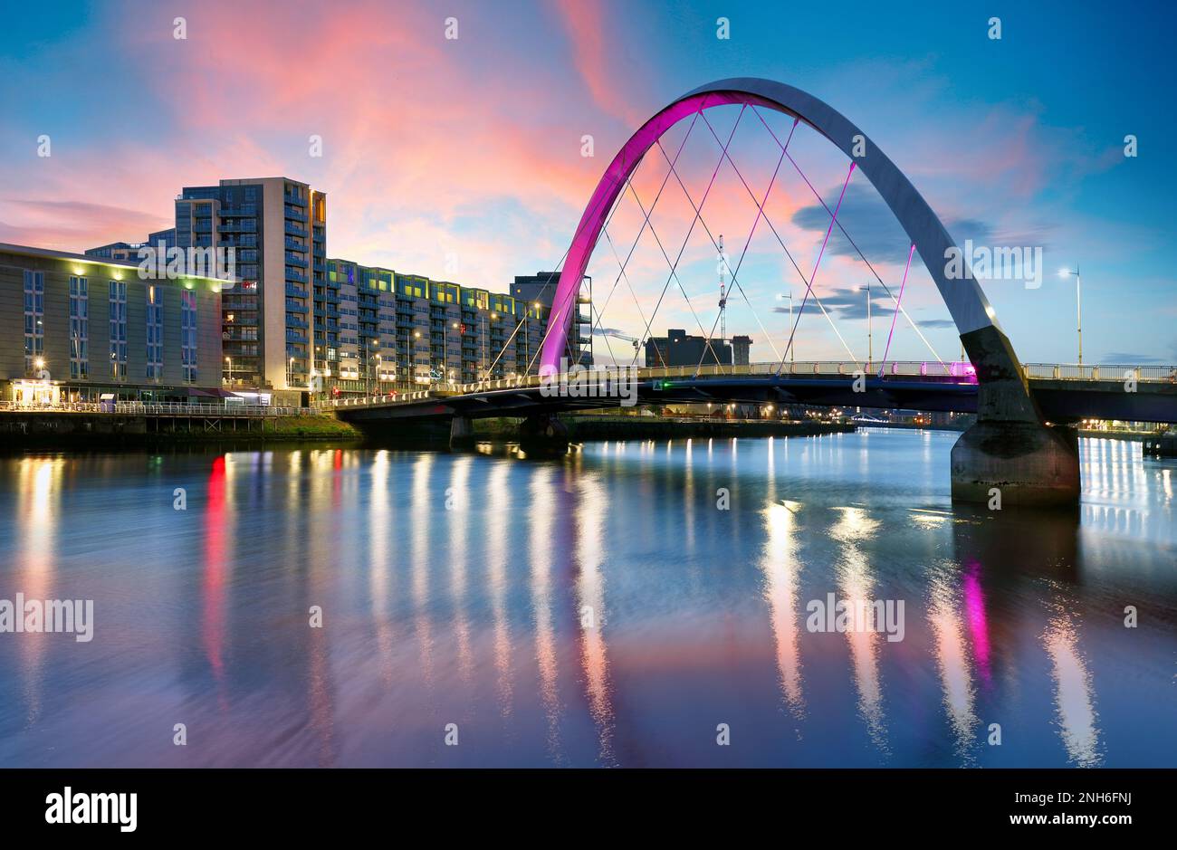 Beautiful Sunset Clyde Arc Bridge across river in Glasgow, Scotland, UK. It is nice weather with reflection on water, blue sky, lights from buildings Stock Photo