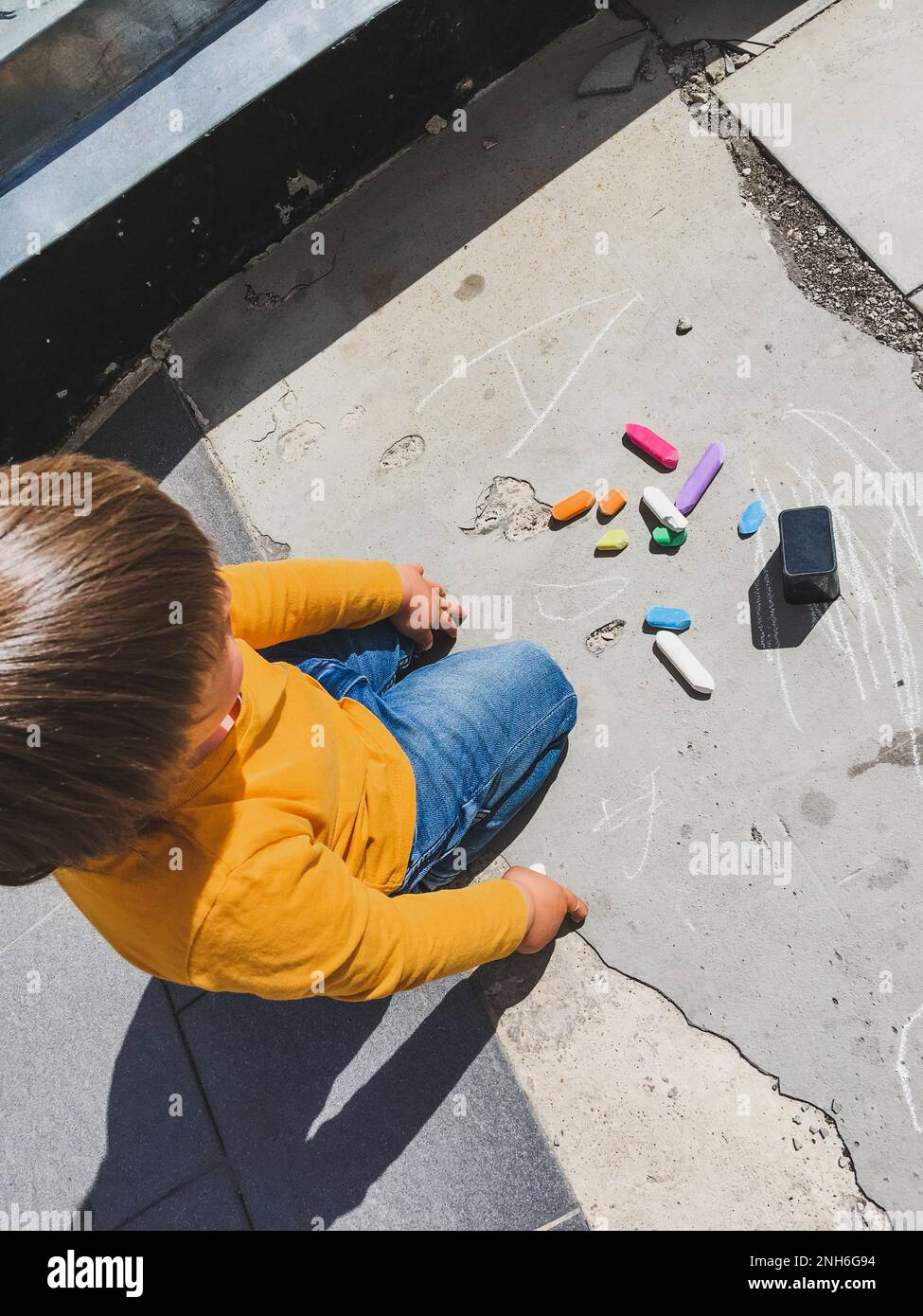 Toddler in jeans draws with crayons on the asphalt in sunny day. Child ...